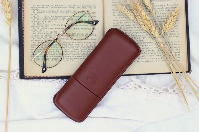 brown leather glasses case on an old open book and gold glasses next to it