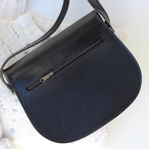 Puede incluir: Bolso bandolera de cuero negro con un bolsillo con cremallera en la parte posterior.