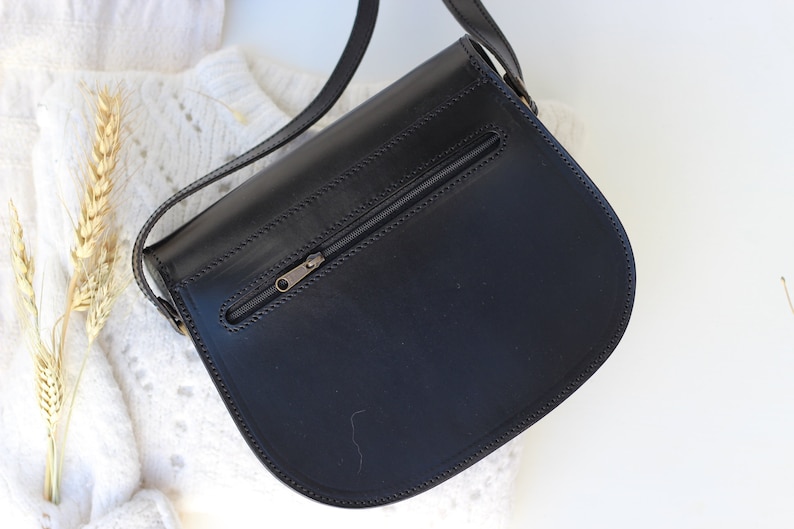 Puede incluir: Bolso bandolera de cuero negro con un bolsillo con cremallera en la parte posterior.