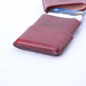 May include: A burgundy leather card holder with a black trim, open to reveal several credit cards. The wallet is rectangular with rounded edges and a stitched border. The background is white.