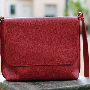 May include: A red leather messenger bag with a flap closure and a gold metal clasp. The bag has a small embossed letter "B" on the front.
