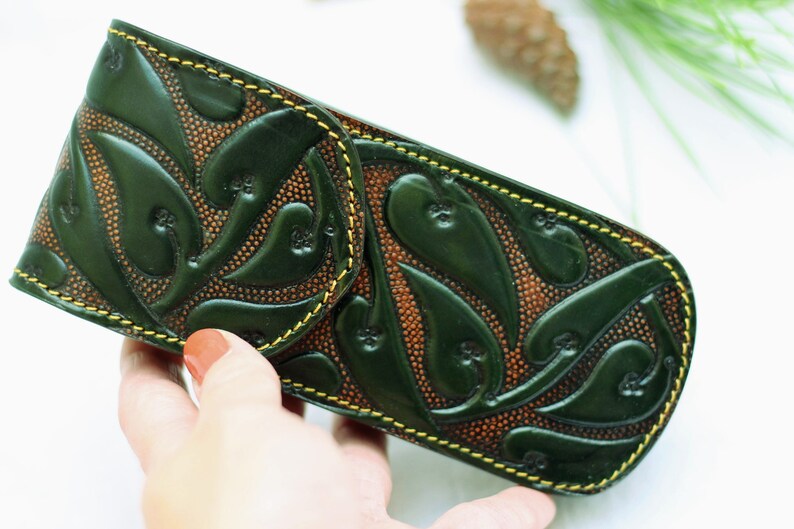 May include: A green leather pencil case with a floral design and yellow stitching.