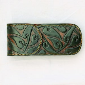 May include: A green leather case with a brown embossed pattern of leaves and swirls. The case has a yellow stitch around the edges.