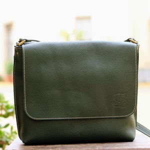 May include: A dark green leather messenger bag with a flap closure and a small embossed logo on the front.