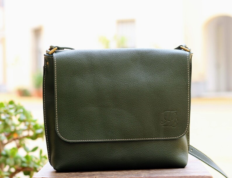 May include: A dark green leather messenger bag with a flap closure and a small embossed logo on the front.