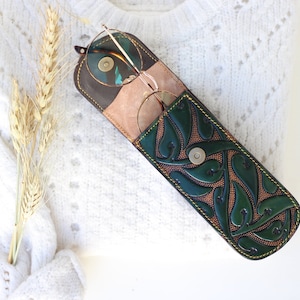 May include: A green leather glasses case with a floral design and a snap closure. The case is open and a pair of glasses is inside.