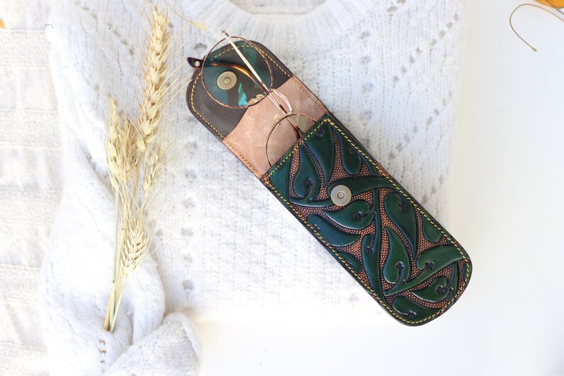 May include: A green leather glasses case with a floral design and a snap closure. The case is open and a pair of glasses is inside.