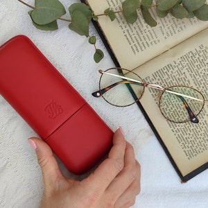 red leather glasses case with talabar logo engraved on it, a woman's hand holds the glasses case over an old open book