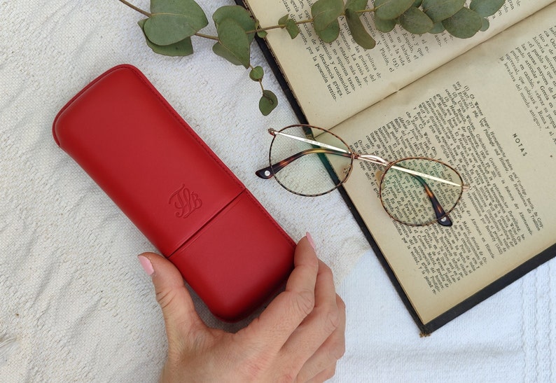 red leather glasses case with talabar logo engraved on it, a woman's hand holds the glasses case over an old open book