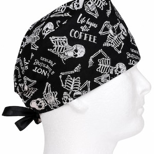 May include: Black surgical scrub cap with a repeating white skeleton and coffee-themed text pattern. The text includes "Life begins after COFFEE" and "NOT a morning person". The cap has a black tie closure.