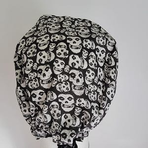 May include: A black and white skull print bouffant style cap. The cap is covered in a repeating pattern of white skulls on a black background. The cap is gathered at the base and appears to be made of fabric.