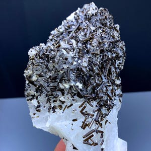 May include: A natural mineral specimen featuring a cluster of dark brown, needle-like crystals atop a translucent, white crystalline base. The crystals are densely packed, creating a textured surface. The overall form is irregular and jagged.