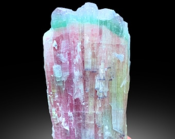 May include: A multi-colored tourmaline crystal with pink, green, and blue hues. The crystal is translucent and has a striated surface. It is a natural gemstone.