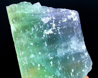 May include: A large, translucent green and white crystal with a striated surface. The crystal has a slightly iridescent sheen.