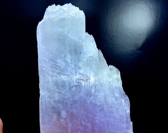 May include: A large, translucent, purple and blue selenite crystal with striations. The crystal is smooth and has a natural, rough edge.