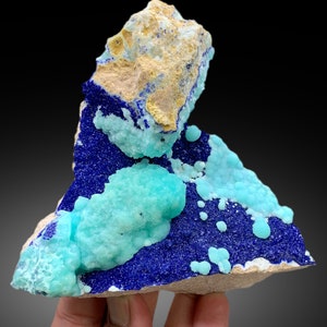 May include: A cluster of blue azurite and green chrysocolla crystals on a matrix of light brown rock. The crystals are arranged in a random pattern, with some of the azurite crystals forming small, rounded shapes.