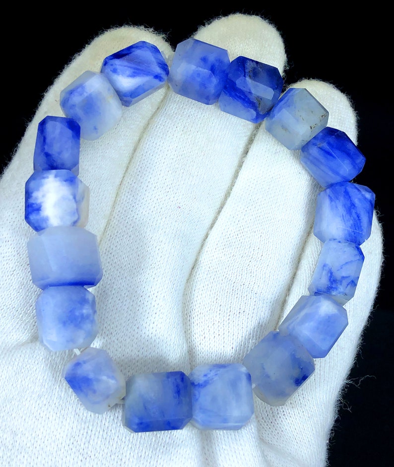 May include: A blue and white gemstone bracelet with faceted beads. The bracelet is made of natural stone and has a unique, marbled pattern.