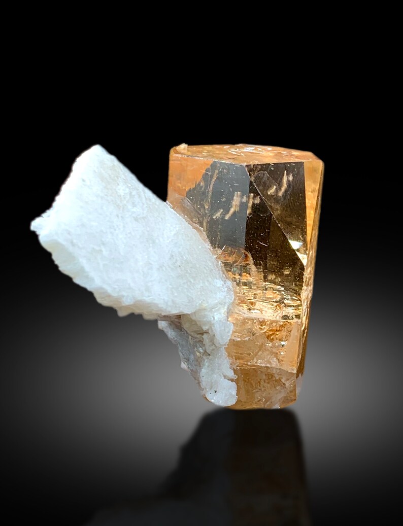 May include: A large, clear, orange-brown topaz crystal with a white, opaque, mineral matrix.