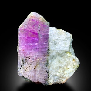 May include: A large, purple and white crystal with a striated texture. The crystal is embedded in a white, rocky matrix.