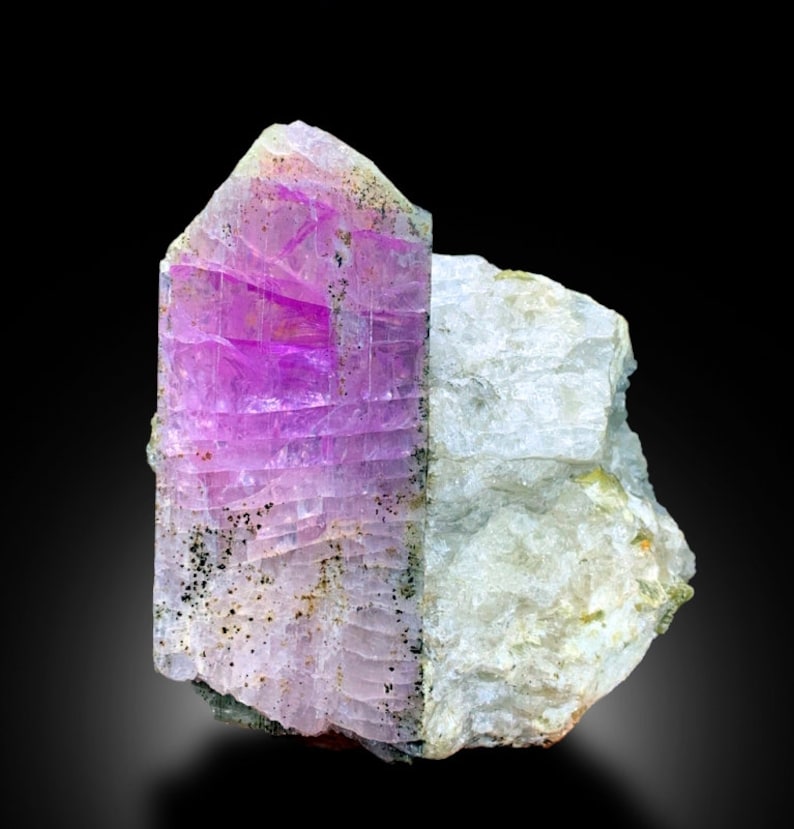May include: A large, purple and white crystal with a striated texture. The crystal is embedded in a white, rocky matrix.
