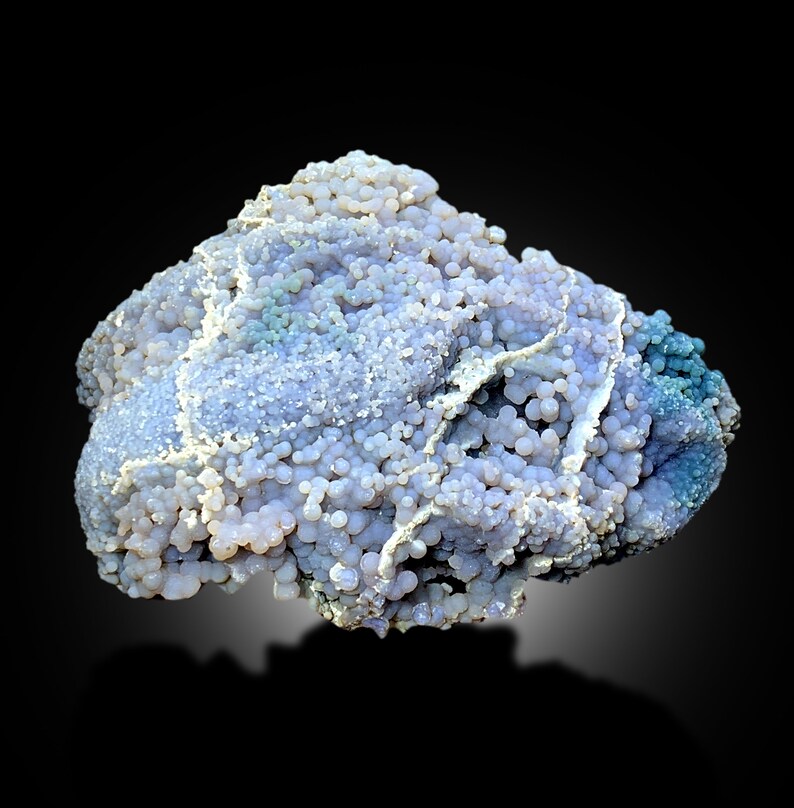 May include: A large, irregularly shaped, purple and blue agate with a textured surface. The agate is covered in small, round nodules.