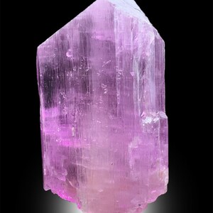 Puede incluir: Un gran cristal rosa transl&uacute;cido con estr&iacute;as. El cristal tiene forma de prisma y tiene una punta afilada en la parte superior.