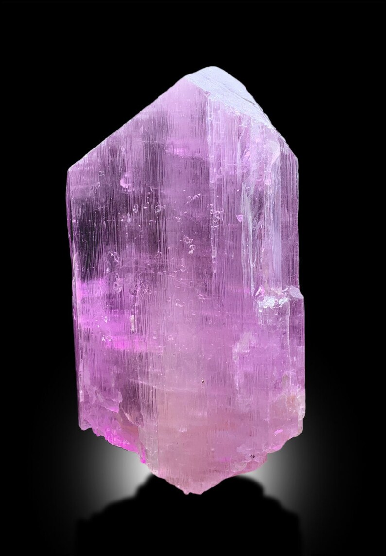 Puede incluir: Un gran cristal rosa transl&uacute;cido con estr&iacute;as. El cristal tiene forma de prisma y tiene una punta afilada en la parte superior.
