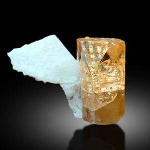 May include: A large, clear, orange-brown topaz crystal with a white, opaque matrix. The crystal is faceted and has a glassy luster.