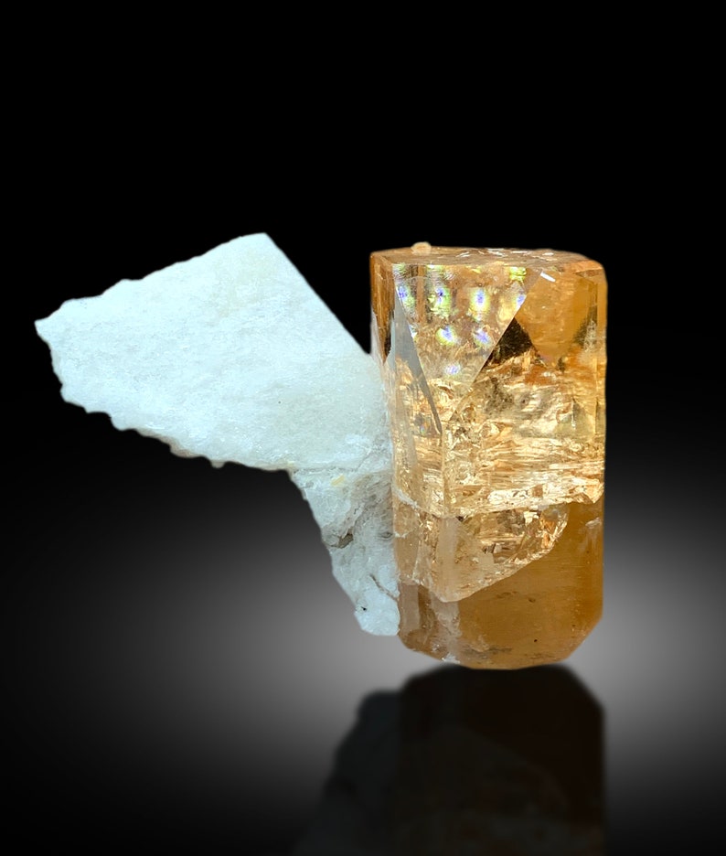 May include: A large, clear, orange-brown topaz crystal with a white, opaque matrix. The crystal is faceted and has a glassy luster.