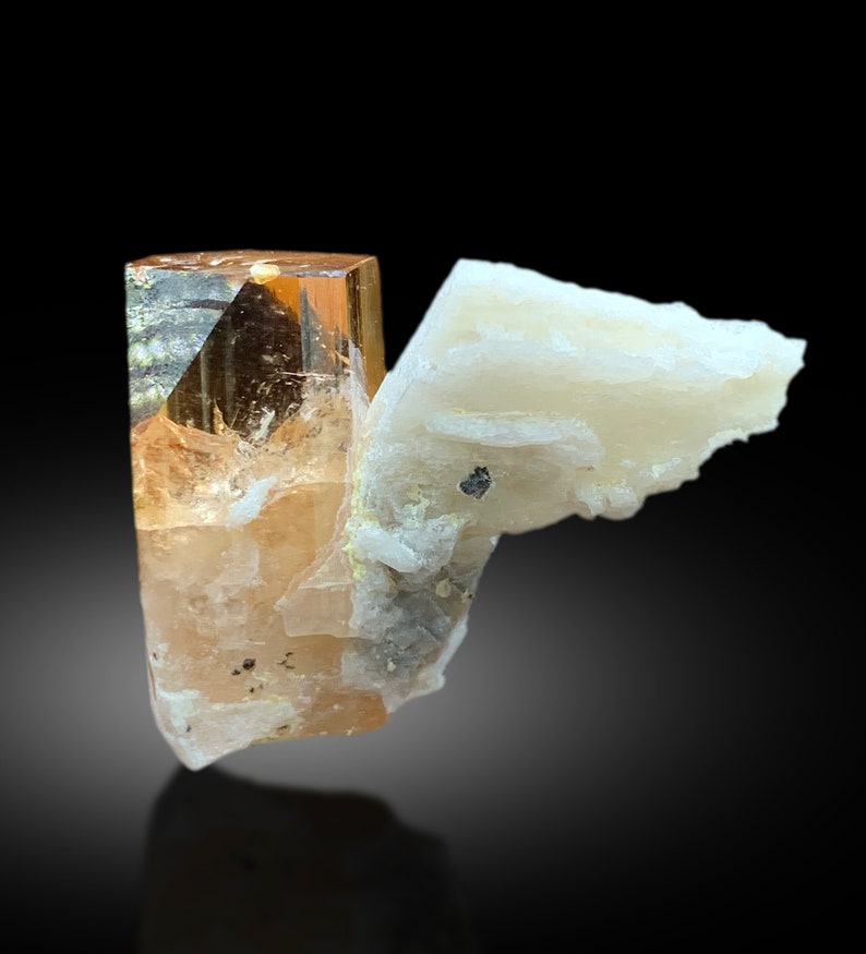 May include: A translucent, orange-brown topaz crystal with a white, layered mineral matrix. The crystal is sharp and well-defined, with a slight golden hue.
