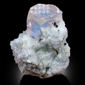Puede incluir: Un cristal azul claro iridiscente de forma hexagonal, rodeado de una matriz de cristales blancos m&aacute;s peque&ntilde;os.