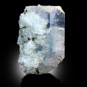 Puede incluir: Un gran cristal transparente azul claro con un acabado brillante. El cristal est&aacute; cubierto de cristales blancos m&aacute;s peque&ntilde;os. El cristal se coloca sobre un fondo negro.
