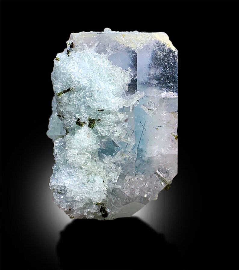 Puede incluir: Un gran cristal transparente azul claro con un acabado brillante. El cristal est&aacute; cubierto de cristales blancos m&aacute;s peque&ntilde;os. El cristal se coloca sobre un fondo negro.