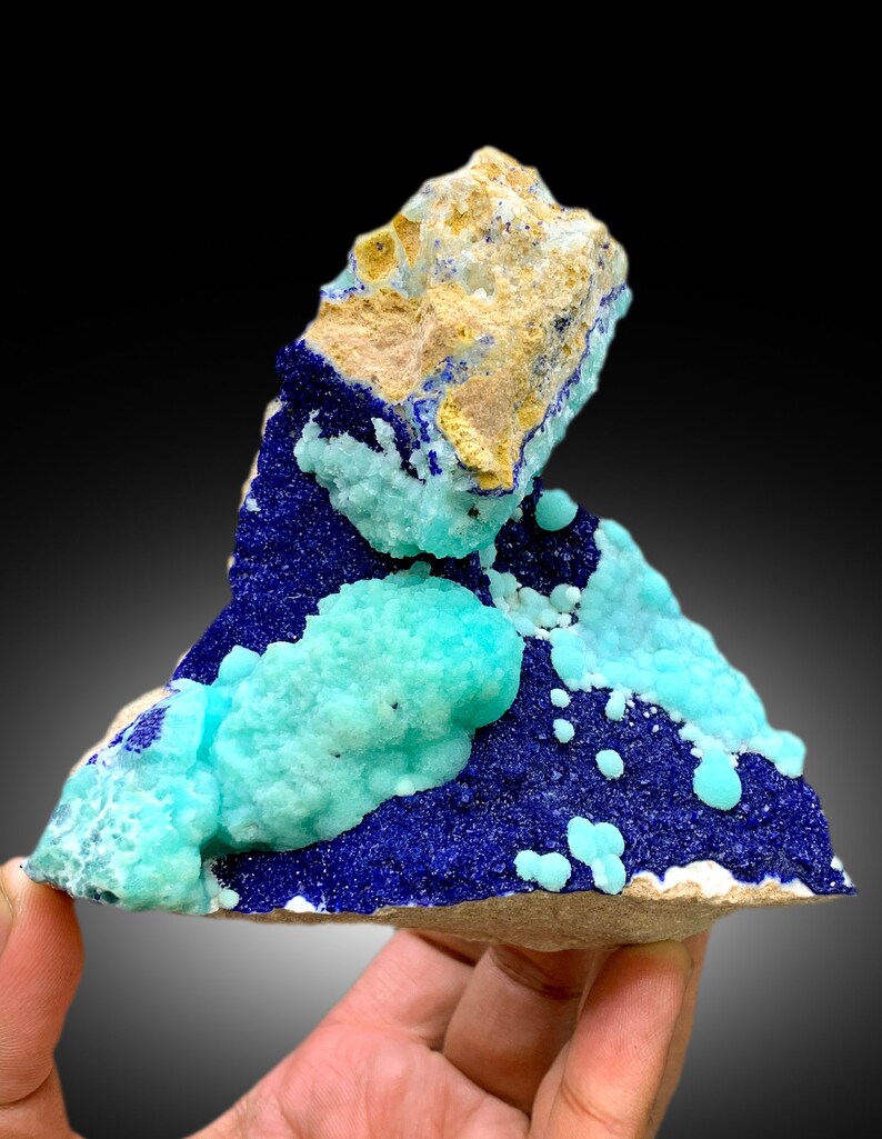 May include: A cluster of blue azurite and green chrysocolla crystals on a matrix of tan rock. The crystals are arranged in a visually appealing way, creating a unique and beautiful specimen.