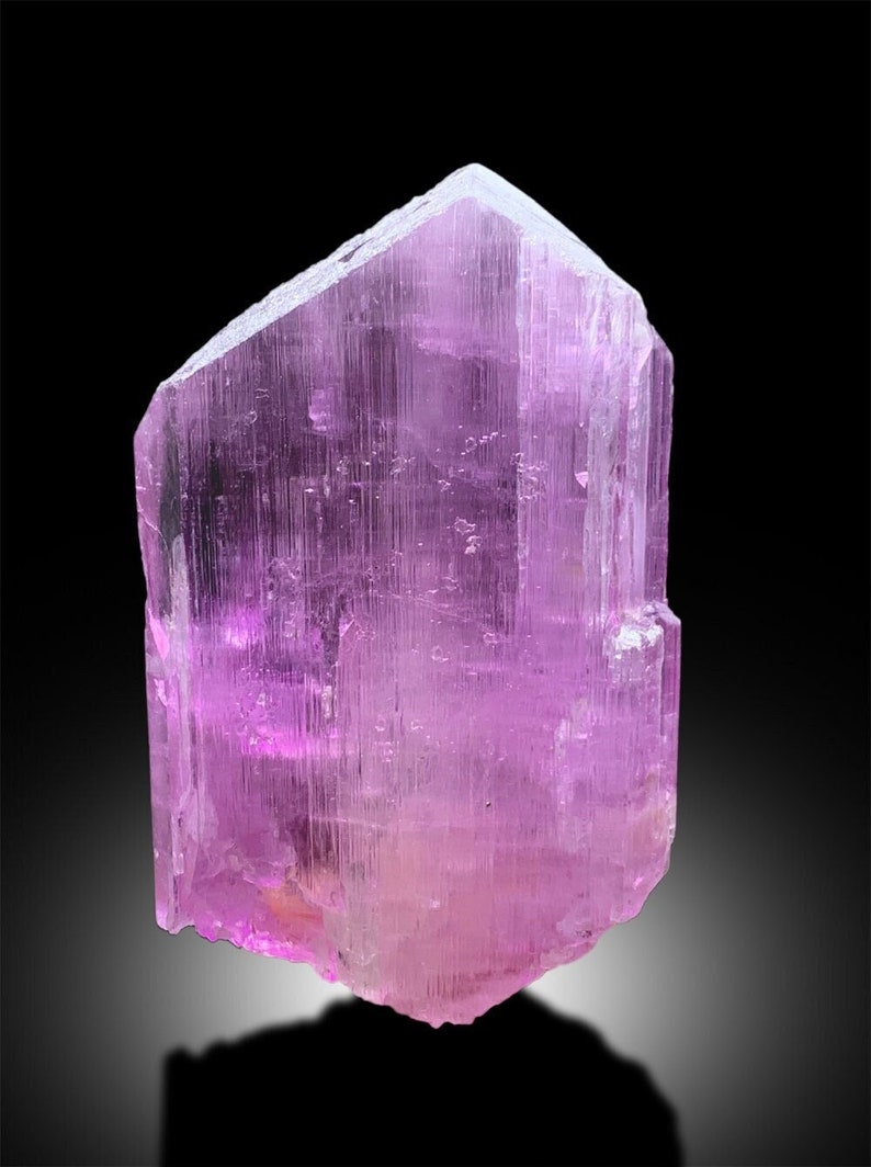 Puede incluir: Un gran cristal rosa transl&uacute;cido con una forma geom&eacute;trica facetada. El cristal tiene una superficie lisa y pulida y est&aacute; iluminado por una luz suave.