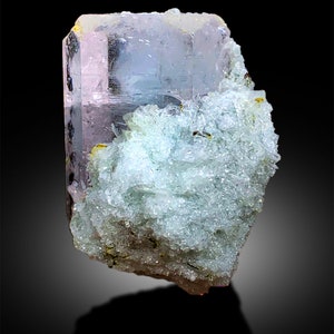 Puede incluir: Un gran cristal transparente, rosa y azul con una matriz rugosa, blanca y verde. El cristal tiene forma de prisma con muchas facetas.
