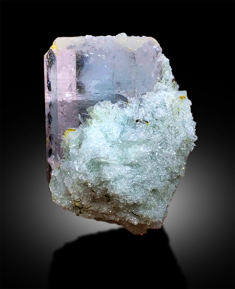 Puede incluir: Un gran cristal transparente, rosa y azul con una matriz rugosa, blanca y verde. El cristal tiene forma de prisma con muchas facetas.