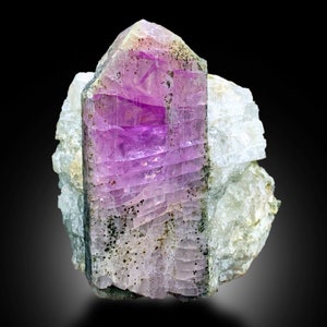 May include: A large, purple, and green crystal with a striated surface. The crystal is embedded in a white, rocky matrix.