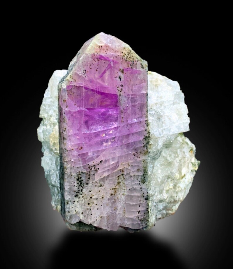 May include: A large, purple, and green crystal with a striated surface. The crystal is embedded in a white, rocky matrix.