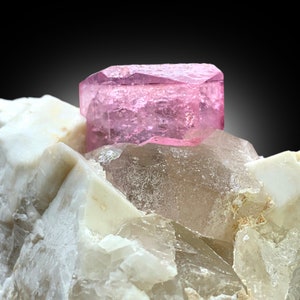 May include: A pink, faceted, gem crystal sits atop a cluster of white and clear quartz crystals.
