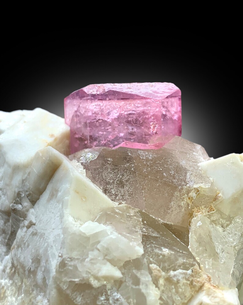 May include: A pink, faceted, gem crystal sits atop a cluster of white and clear quartz crystals.