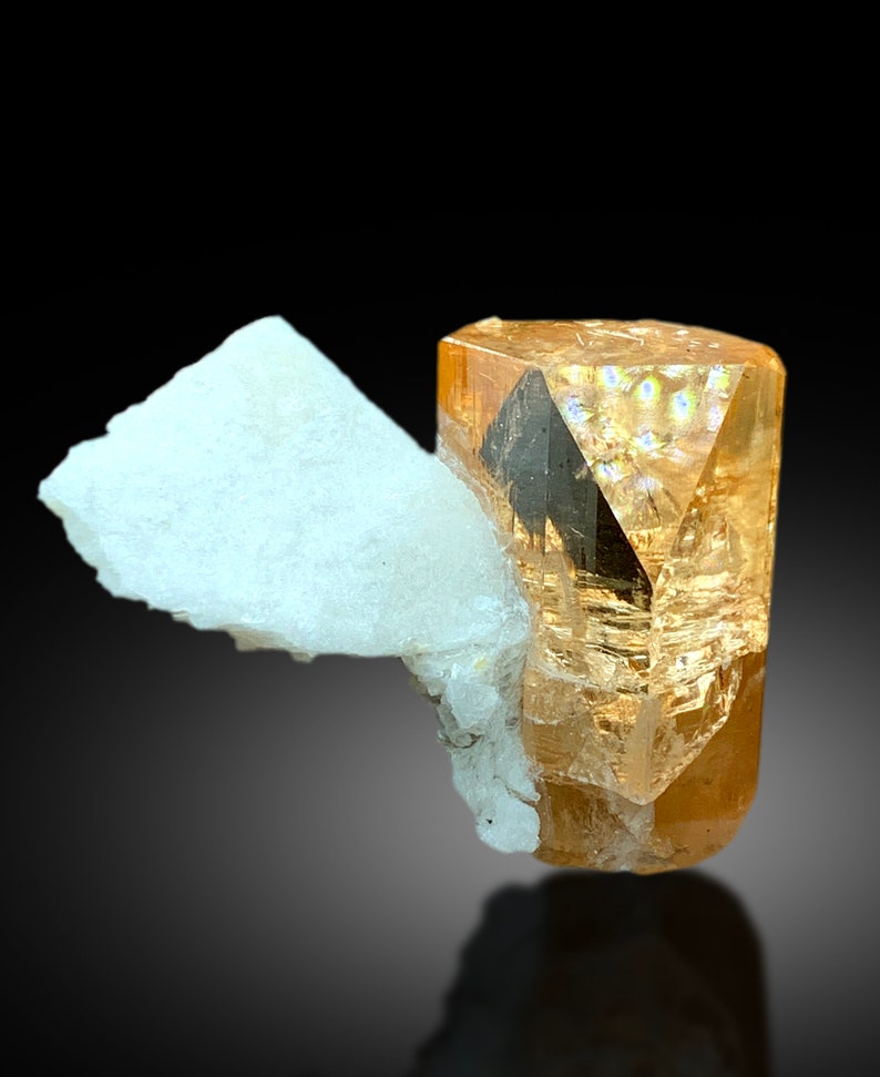 May include: A large, clear, orange-brown topaz crystal with a sharp, pointed termination. The crystal is sitting on a bed of white, opaque, crystalline material.