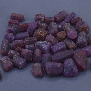 Könnte beinhalten: Ein Haufen roter und violetter Rubingesteine. Die Edelsteine sind roh und unpoliert und haben alle unterschiedliche Größen und Formen.