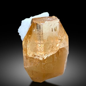 May include: A large, clear, light brown topaz crystal with a faceted, geometric shape.