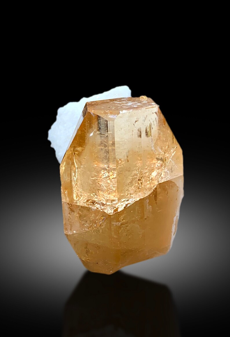May include: A large, clear, light brown topaz crystal with a faceted, geometric shape.