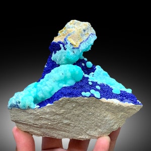 May include: A cluster of blue and turquoise mineral specimens on a gray rock. The mineral crystals are arranged in a visually appealing way, creating a unique and interesting display.