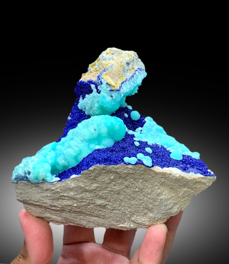 May include: A cluster of blue and turquoise mineral specimens on a gray rock. The mineral crystals are arranged in a visually appealing way, creating a unique and interesting display.