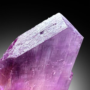 Puede incluir: Un gran cristal p&uacute;rpura transl&uacute;cido con estr&iacute;as en su superficie. El cristal tiene forma de prisma con una punta afilada en la parte superior.