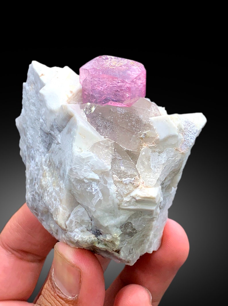 May include: A pink tourmaline crystal on a white matrix of rock. The crystal is faceted and has a translucent appearance.