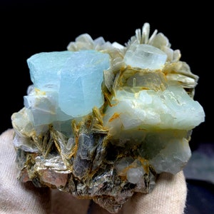 May include: A cluster of aquamarine crystals with a light blue color, embedded in a matrix of gray and brown mica. The crystals have a glassy luster and are translucent.